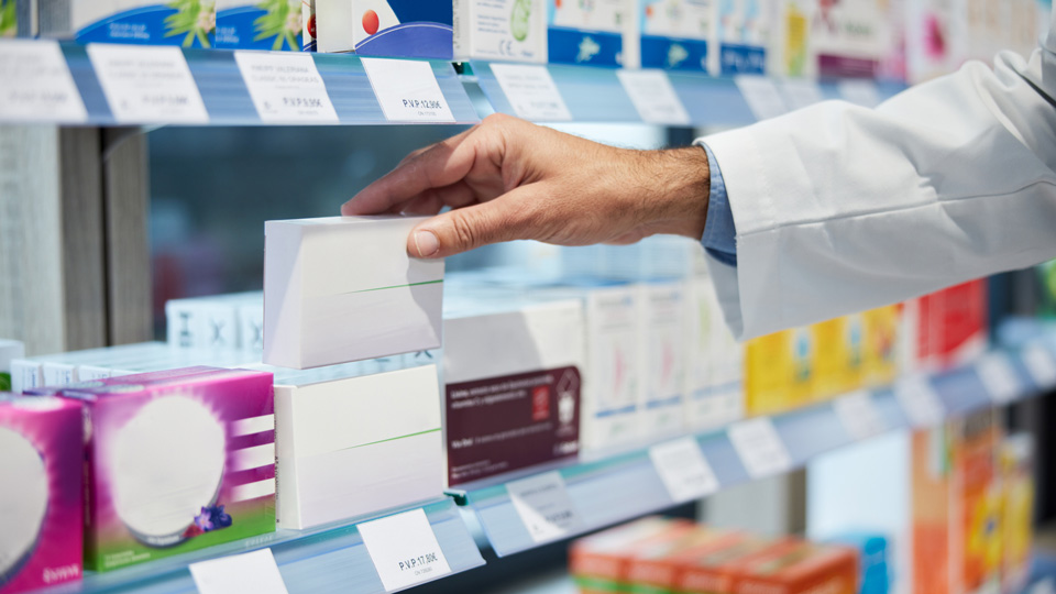A pharmacist places an item on pharmacy shelf