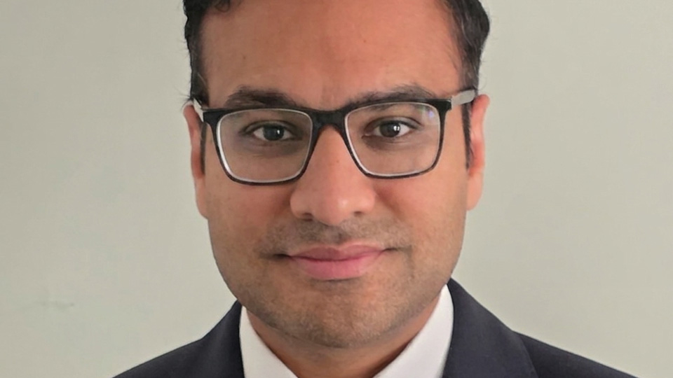 Anish is dressed in a smart suit jacket and photographed against a plain background