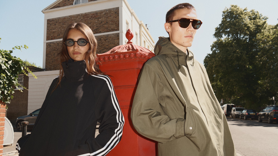 A young man and woman lean irreverently against a traditional red postbox. Both wear parkas and sunglasses