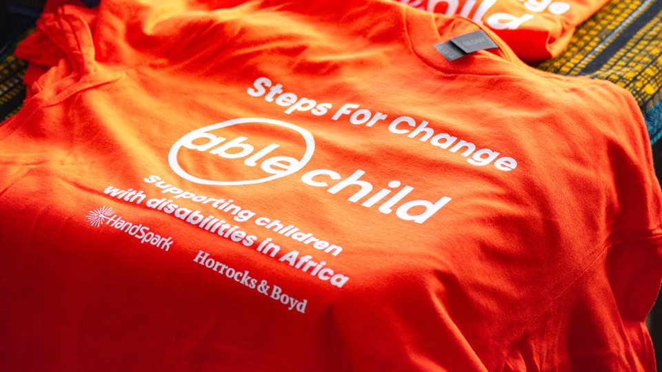 An orange t-shirt for the Steps for Change event. In the centre is a large logo for Able Child. Two smaller logos of the sponsors HandSpark and Horrocks & Boyd are arranged beneath
