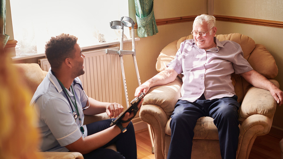 Older man sitting in an armchair and laughing with a care provider
