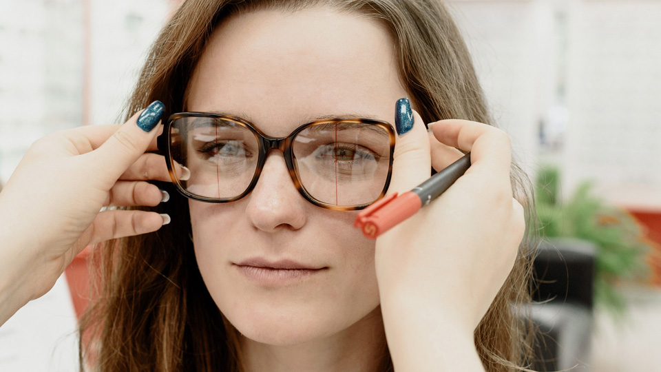A patient sits patiently while a dispensing optician marks up measurements on a pair of lenses