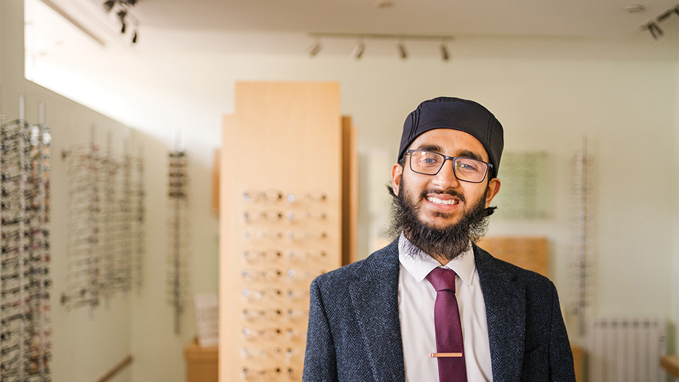 Habeeb is stood smiling in front of a wall of frames