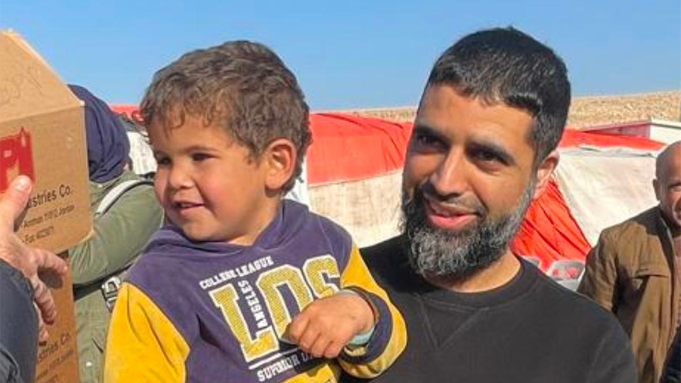 Hammad is holding a small child outside under a blue sky