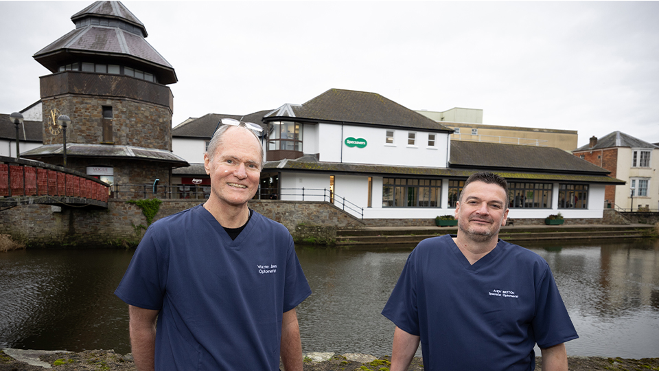 Wayne and Andy are stood by the riverbank outside their practice, weating blue scrubs