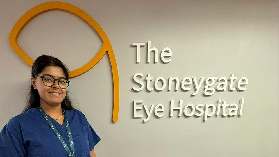 Roshni is stood in front of the Stoneygate Eye Hospital sign indoors 