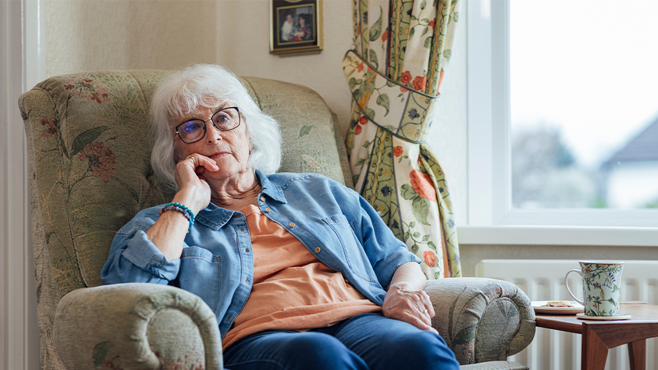 An elderley woman in glasses sits in her chair at home 