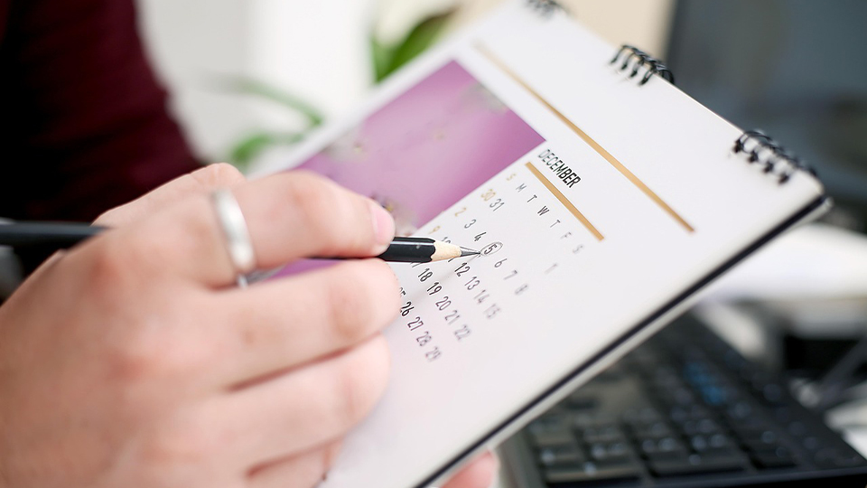 A close up of a hand holding a pencil an circling a date on a calendar 