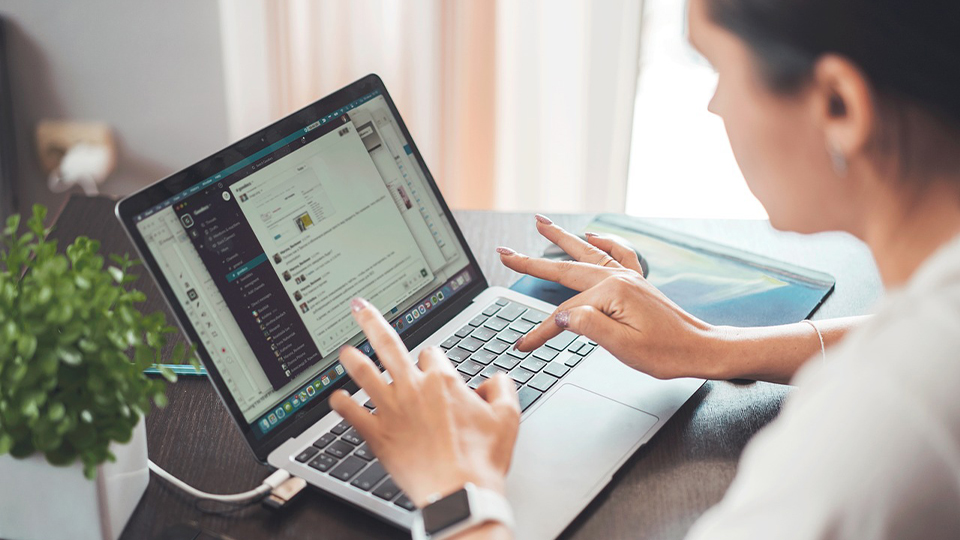 A woman working at a laptop, she is typing on the keyboard and reading through tabs 