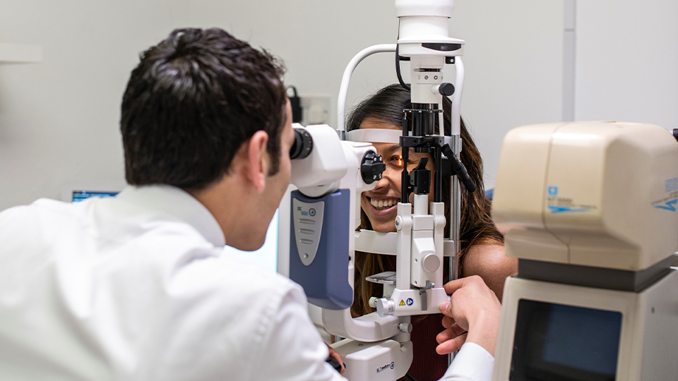 Sian Wilkie laughs as she receives a sight test in practice. The camera is positioned behind the shoulder of the optometrist