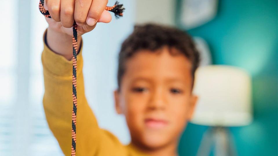 A boy in a yellow jumper holds up a conker on a string