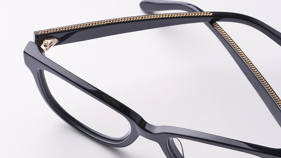 Looking down on the top of a pair of black frames, an inlaid gold chain detail along the arms of the frame is apparent
