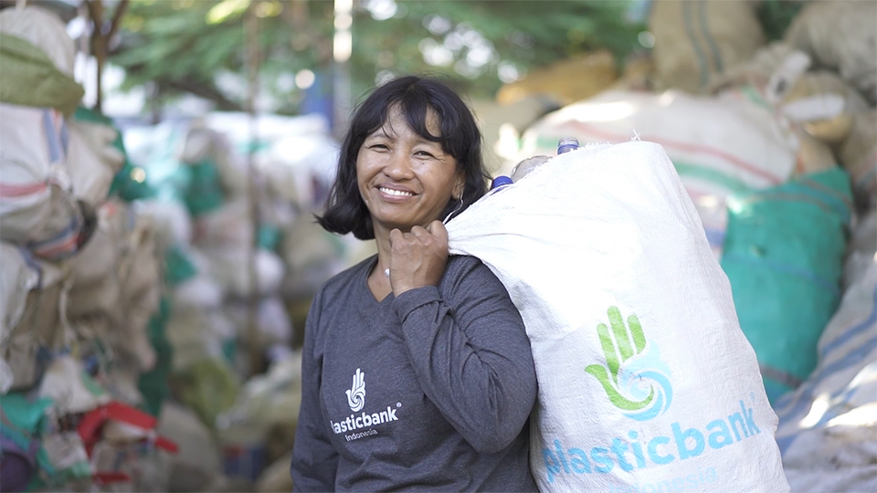 A woman smiles at the camera with a white PlasticBank sack over her shoulder