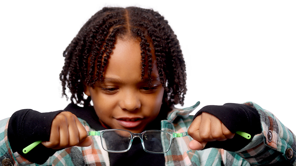 A young boy pulls the arms of his eyewear to show the durability