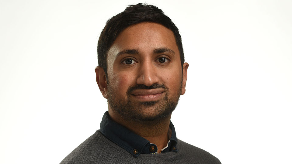 Anish is wearing a grey jumper and looking directly at the camera in a head and shoulders image 
