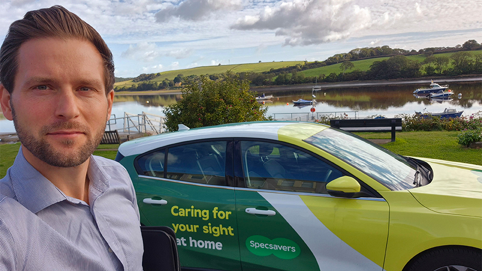 Jason Scaife is pictured holding a folder standing in front of a Specsavers Home Visits vehicle