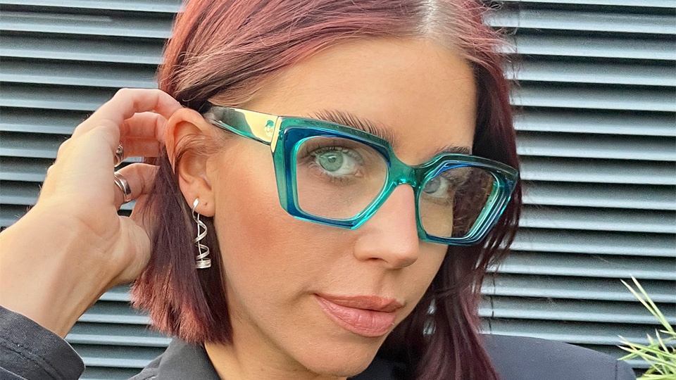 Steph wears chunky acetate ‘Cat’ frames in a translucent blue-green. These contrast against the all-black blazer she wears and enhance the green of her 