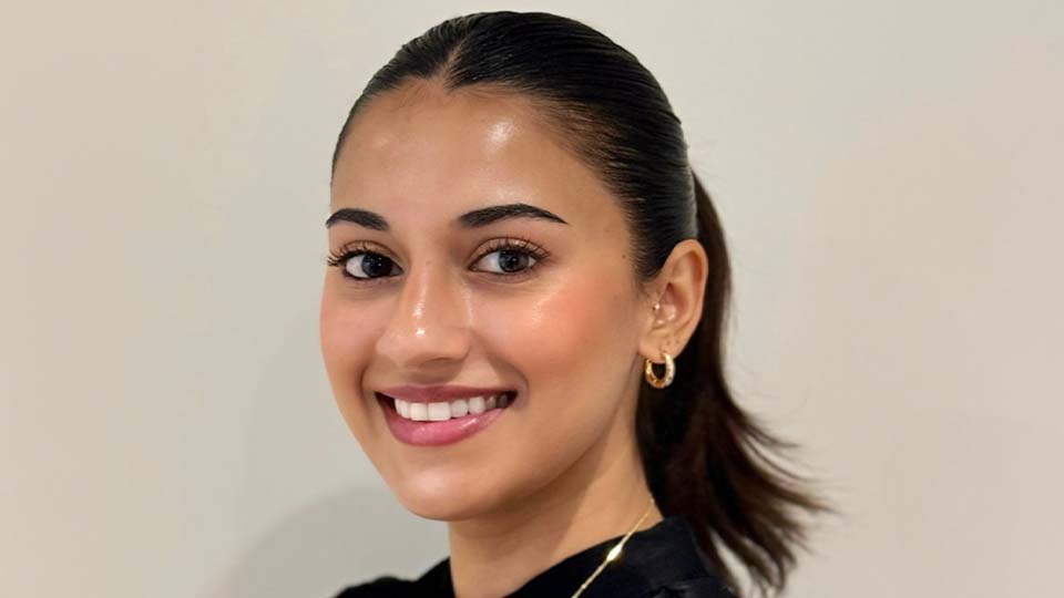  Krupa is wearing a black top and is smiling at the camera whilst facing to the left  