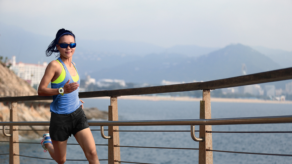 A woman wearing sports attire and Hoya Sportive sunglasses jogs on the seafront