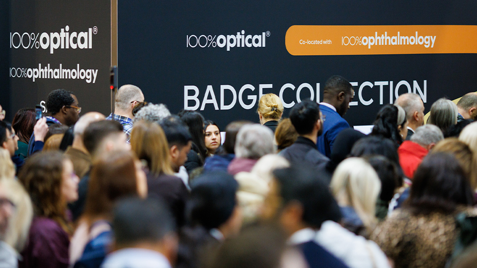 A crowd gathers by the badge collection tables at 100% Optical