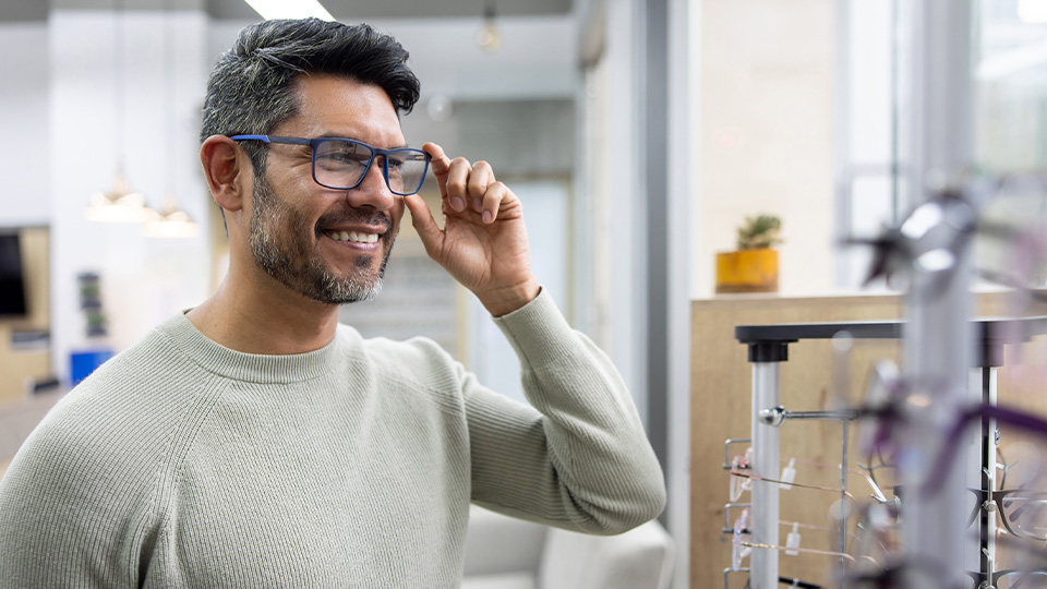 A man tries on blue framed spectacles in an optometry practice