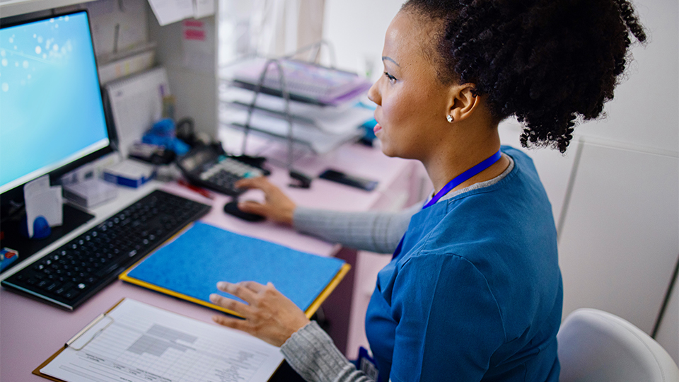 A woman in clinical clothing types at a computer