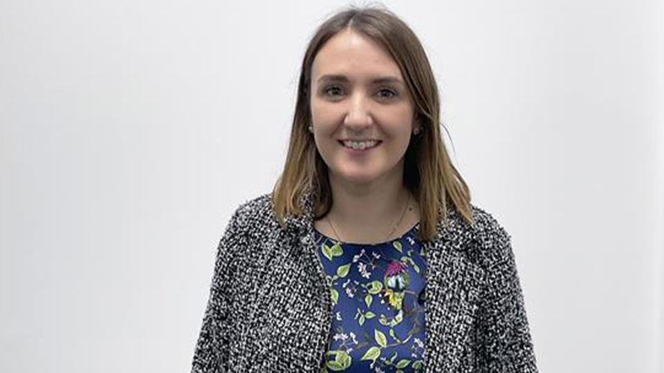Kate stands in front of a white wall, smiling
