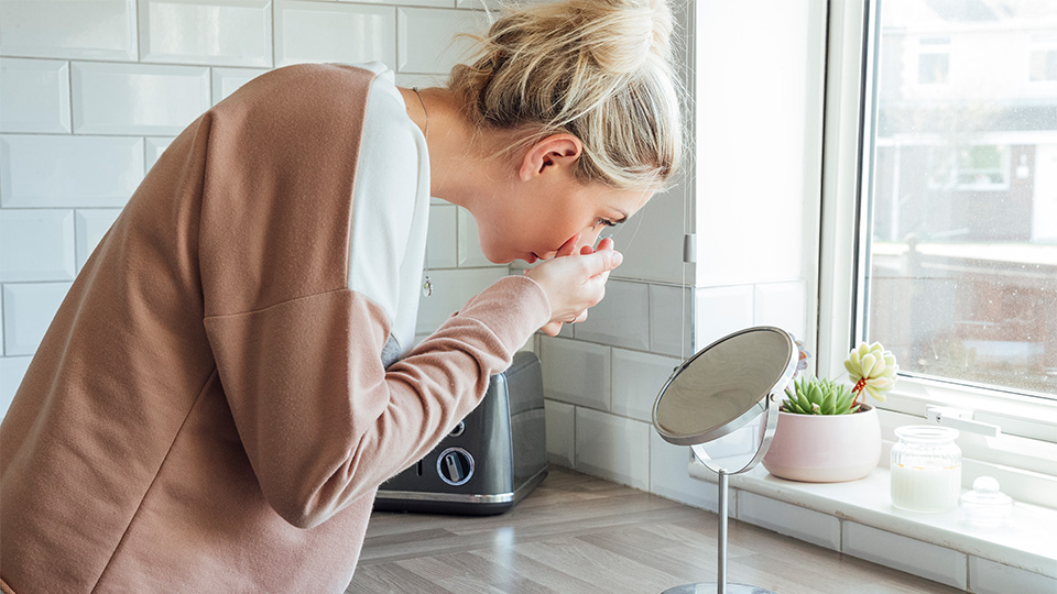 Blonde woman looking in a mirror whilst applying contact lenses