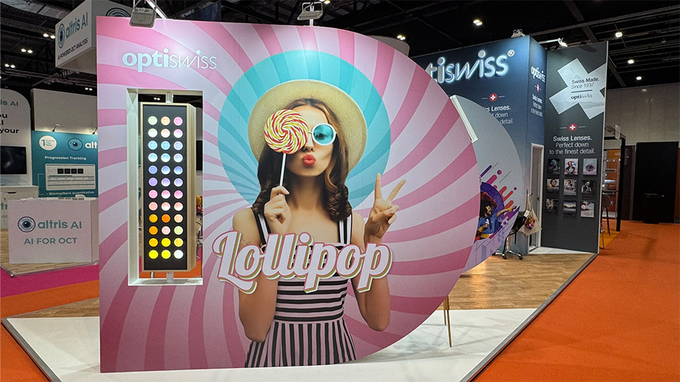 A bright pink and pastel display of Lollipop lens tints at 100% Optical. The display has a picture of a woman holding up a giant swirly lollipop wearing light blue lenses and posing with a pout and peace sign
