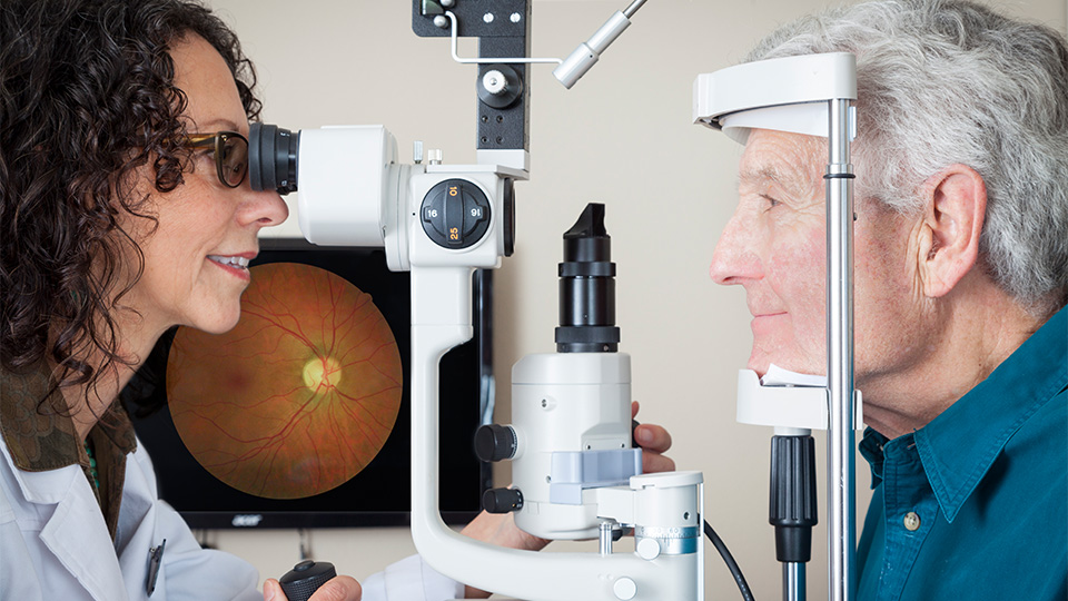 Female optometrist with brown hair performs sight test on an elderly man