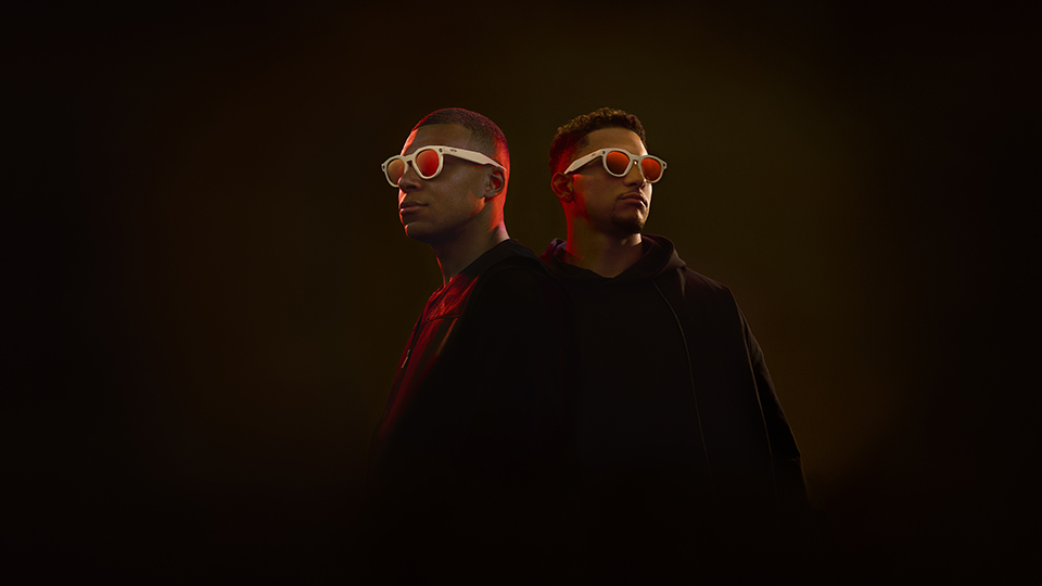 Kylian and Patrick pose together on a dark background, both wearing Oakley Meta HSTN smart eyewear