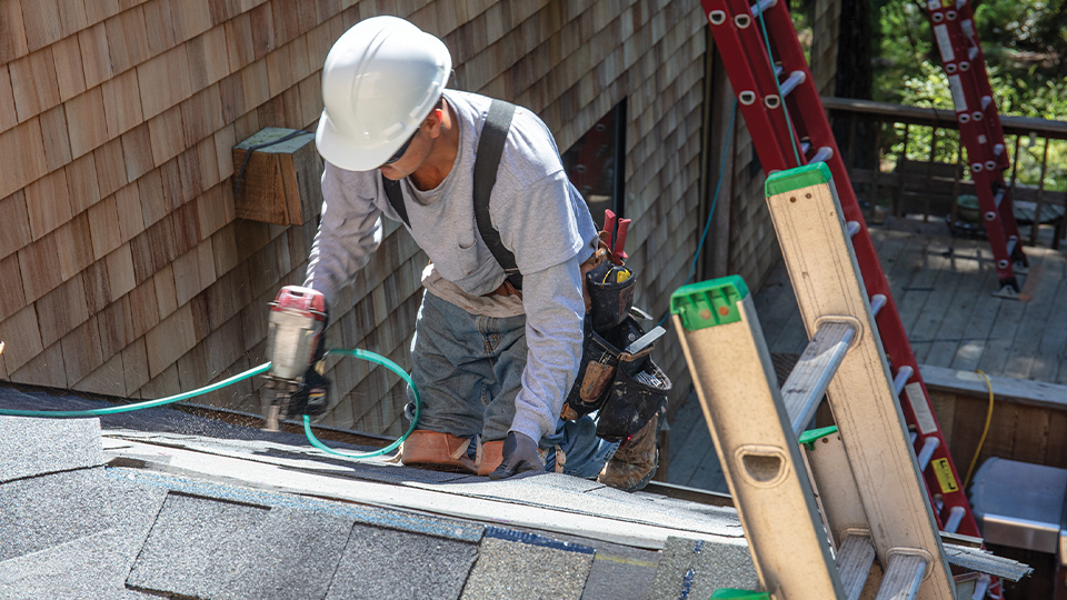 A man in a hard hat works on top of a garage roof