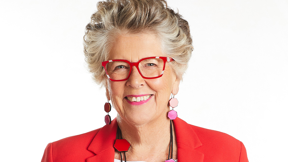 Prue Leith wears a pair of red spectacles with slices of grey. She wears a matching bright red blazer