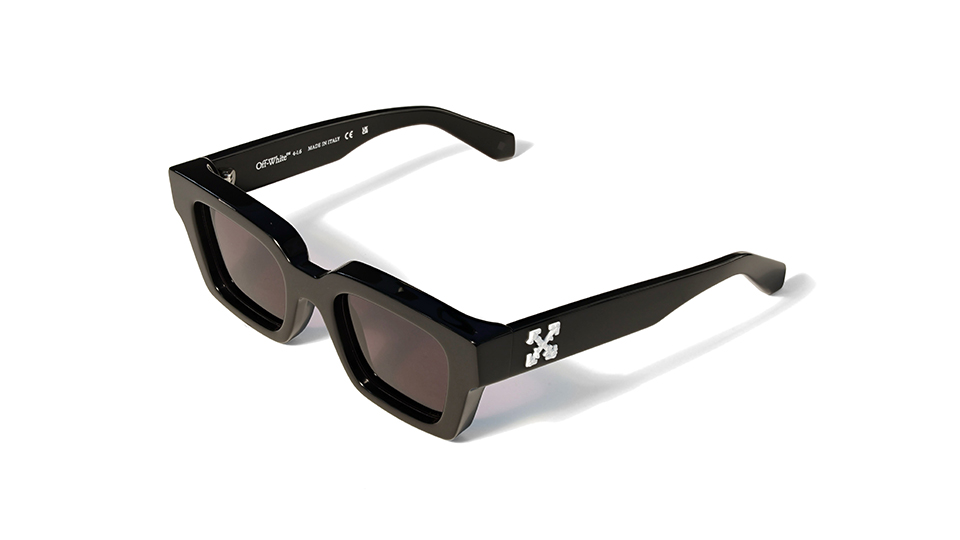 A pair of chunky black sunglasses with dark lenses and a logo of four arrows on the temple