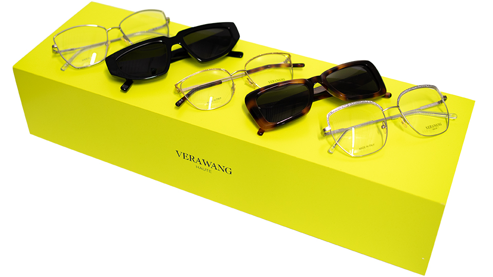 A lime-yellow display base holds five sunglasses and ophthalmic frames