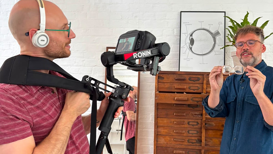 Laurence Derbyshire standing in an eyewear manufacturing spacing holding a camera filming