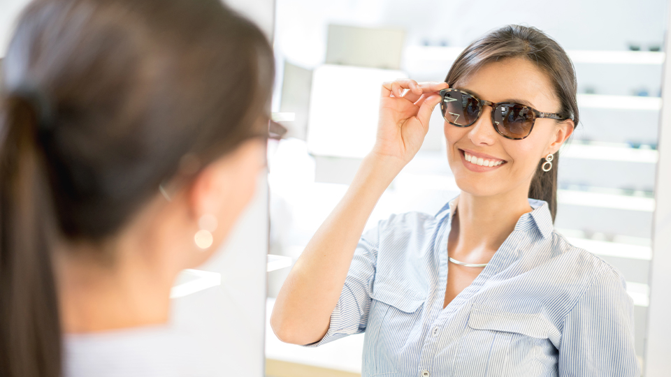 Woman in an opticians standing trying on a pair of sunglasses
