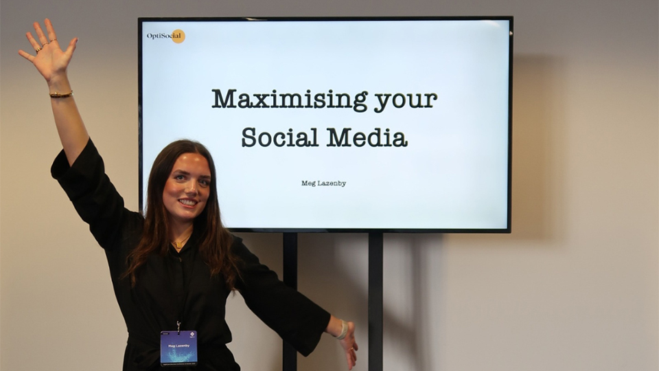 Meg stands in front of a presentation screen reading ‘Maximising your Social Media’
