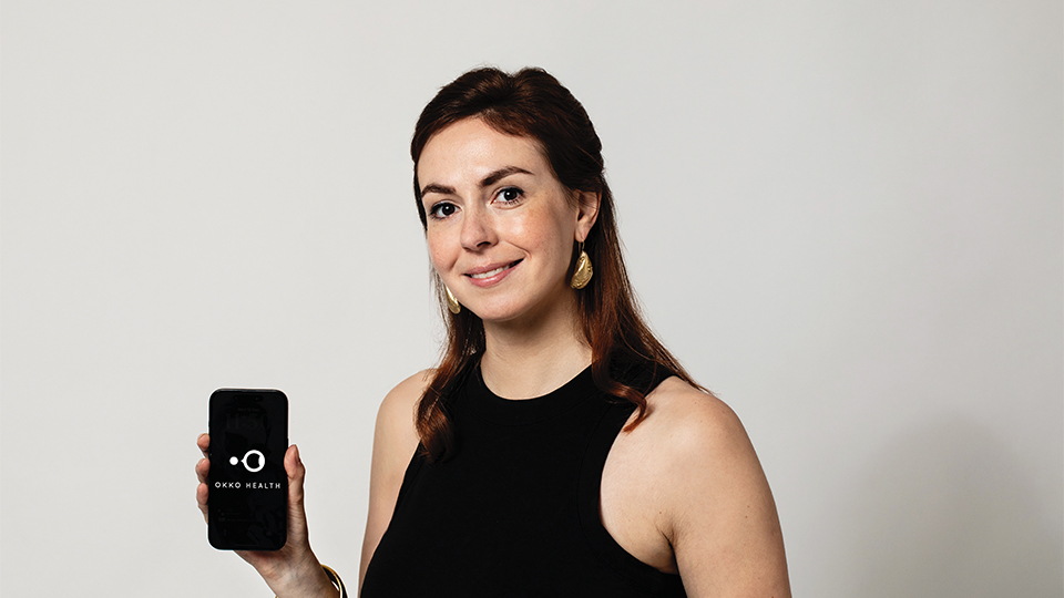 Okko Health founder and optometrist Stephanie Campbell holds a smartphone displaying the Okko Health app