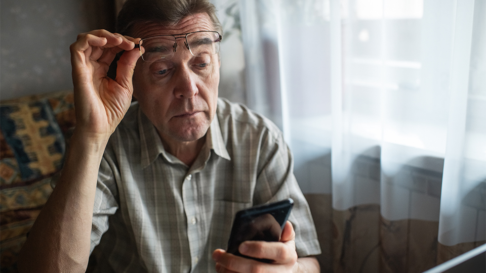 Senior man with bad eyesight looking at smartphone at home