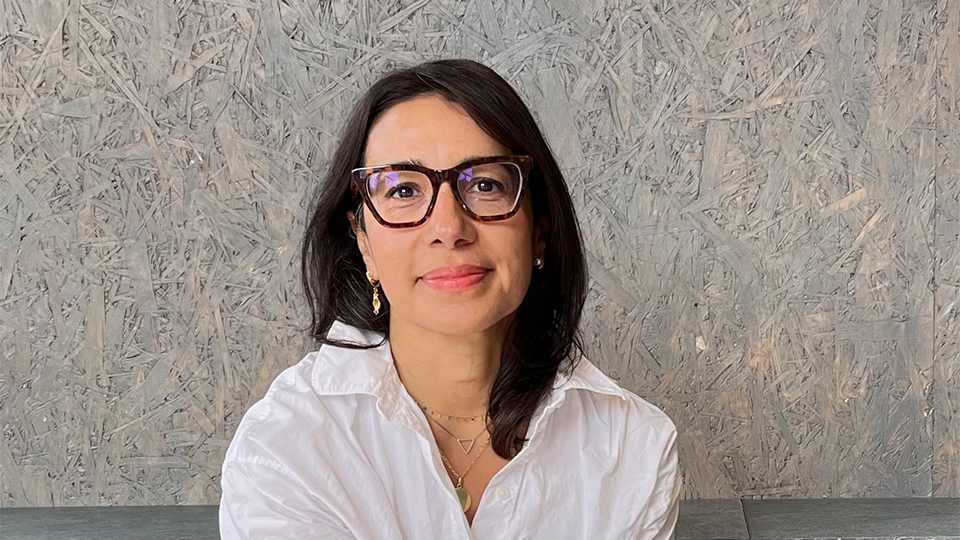 Sandra wears Havana eyewear with an upswept cat’s eye style. She wears a white blouse with striped orange-brown trousers