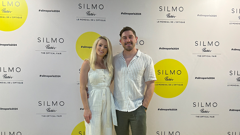 Two people in summer attire pose at a photo wall with the bright yellow branding for Silmo Paris