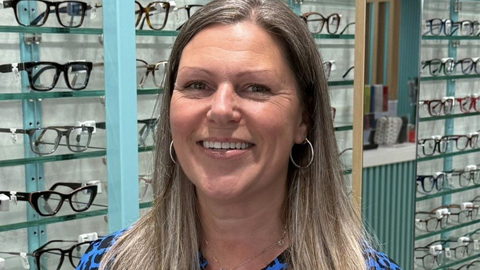 Helen is photographed in the practice. She wears a blue and black leopard-print shirt and rows of frames are in the background