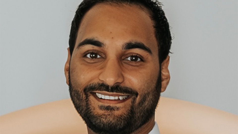 Vikesh smiles side-on to the camera. He wears a white shirt and a pale grey waistcoat and silk tie