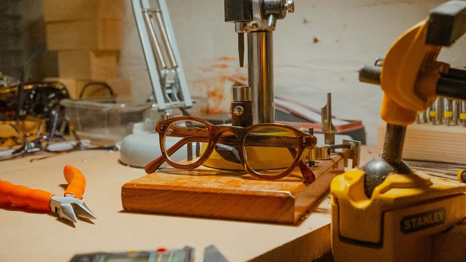 A pair of brown spectacles positioned on a workshop table, surrounded by tools used to make eyewear