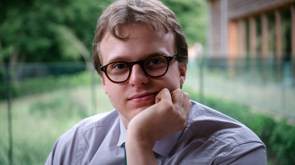 Jake wears tortoiseshell colour spectacles and is photographed in a peaceful garden setting