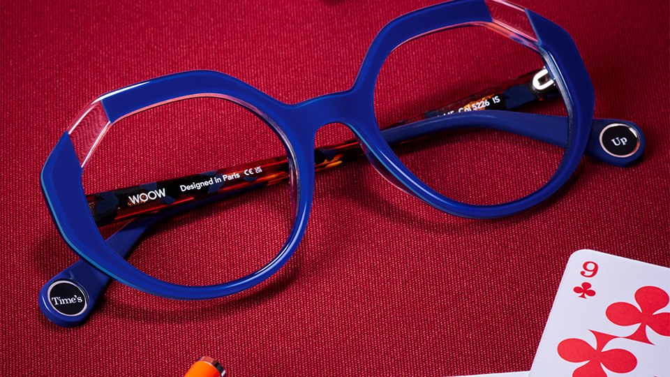 A hexagonal frame in an electric blue with a clear acetate segment creating a ‘cut out’ feature. The inside of each end tip has a sticker reading ‘Time’s’ ‘Up’ and the frame is positioned on a red gambling table, with a red and a blue playing card and dice