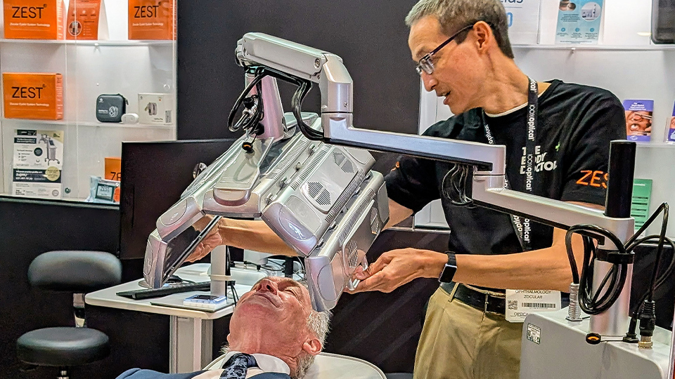 Dr Hilary Jones lies on a treatment chair with a low-level light therapy device positioned over his face. A clinician is carrying out the treatment. The pair are photographed at an exhibition