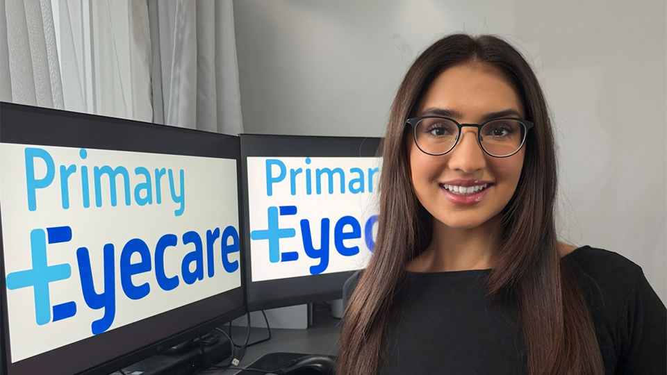 Samiriah Shaikh with computers displaying the Primary Eyecare Services logo in the background