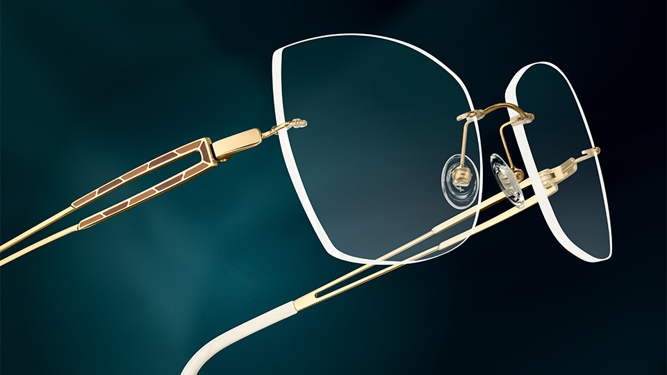 A butterfly shaped pair of glasses with rimless lenses and gold metal arms, featuring lacquer detailing in red and blue
